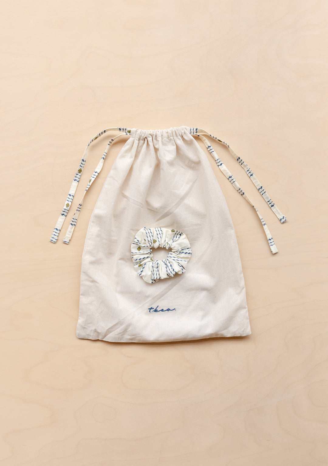 TBCo matching cotton drawstring bag and scrunchie for Cotton Pyjamas in Navy Ditsy floral lying flat on a wooden surface