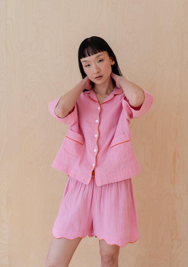 Pink cotton pyjama set from TBCo with scalloped edges and orange piping, showcasing elegant loungewear design on beige backdrop