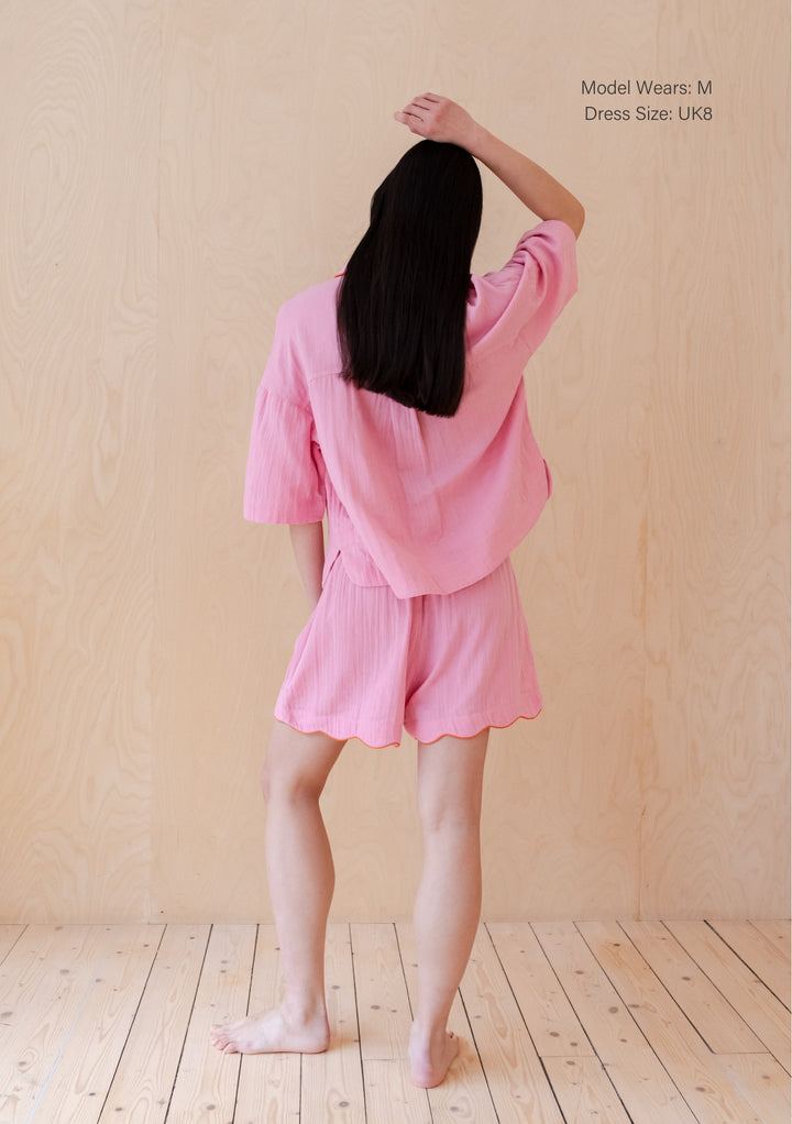 Back view of TBCo Cotton Pyjamas in Pink Scallop featuring scalloped edges and relaxed fit shorts against wooden backdrop