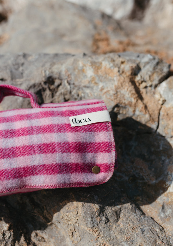 TBCo Recycled Wool Small Picnic Blanket in pink gingham pattern, rolled and secured with popper, displayed on rocky surface