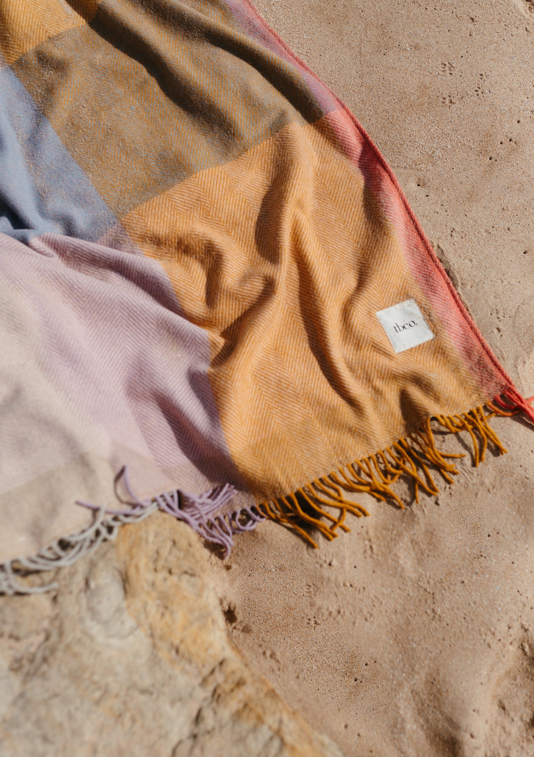 TBCo Recycled Wool Picnic Blanket in Mustard Frame Check displayed with tassels on sandy ground, showing textured weave pattern