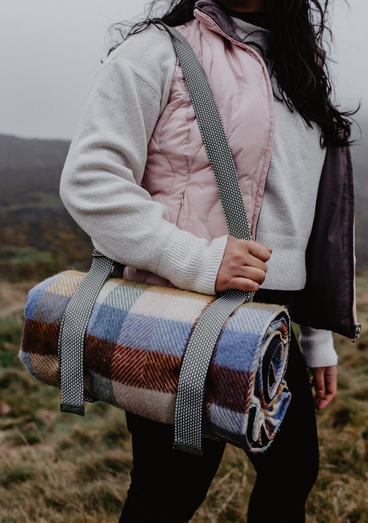 TBCo Recycled Picnic Carrier shown with shoulder strap carrying plaid wool blanket in outdoor countryside setting