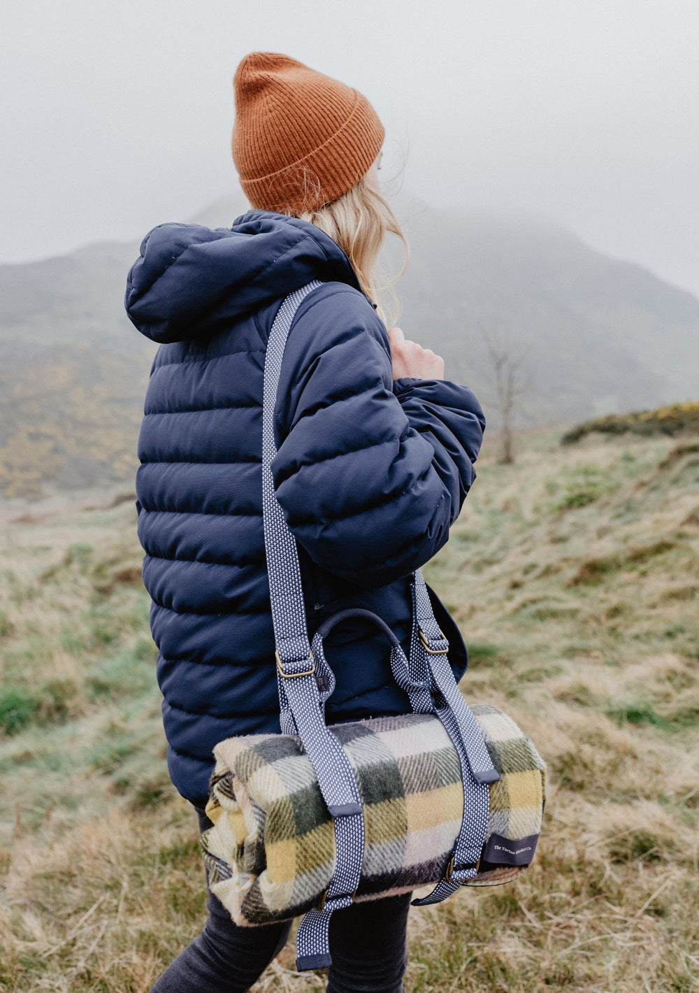 TBCo Recycled Picnic Carrier with adjustable shoulder strap shown on hillside with plaid blanket in sustainable outdoor setting