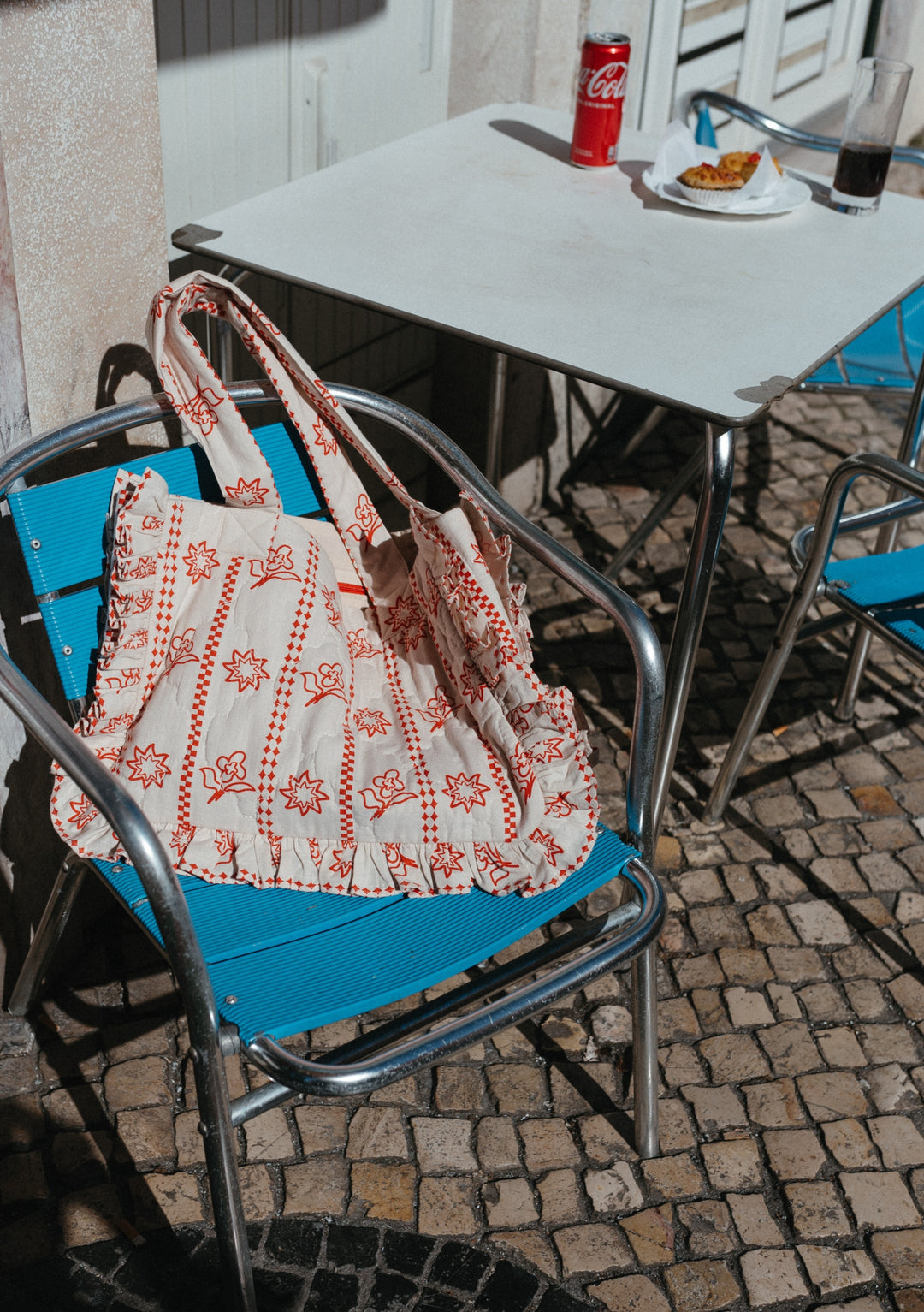 TBCo Quilted Cotton Tote Bag in Flora pattern resting on blue cafe chair, showcasing red floral print against white fabric