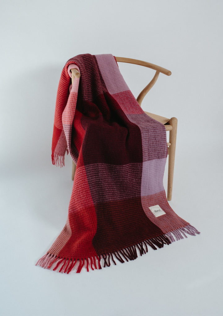 TBCo Recycled Wool Blanket in Burgundy Waffle Block Check draped on wooden chair showing soft fringed texture and cosy colours