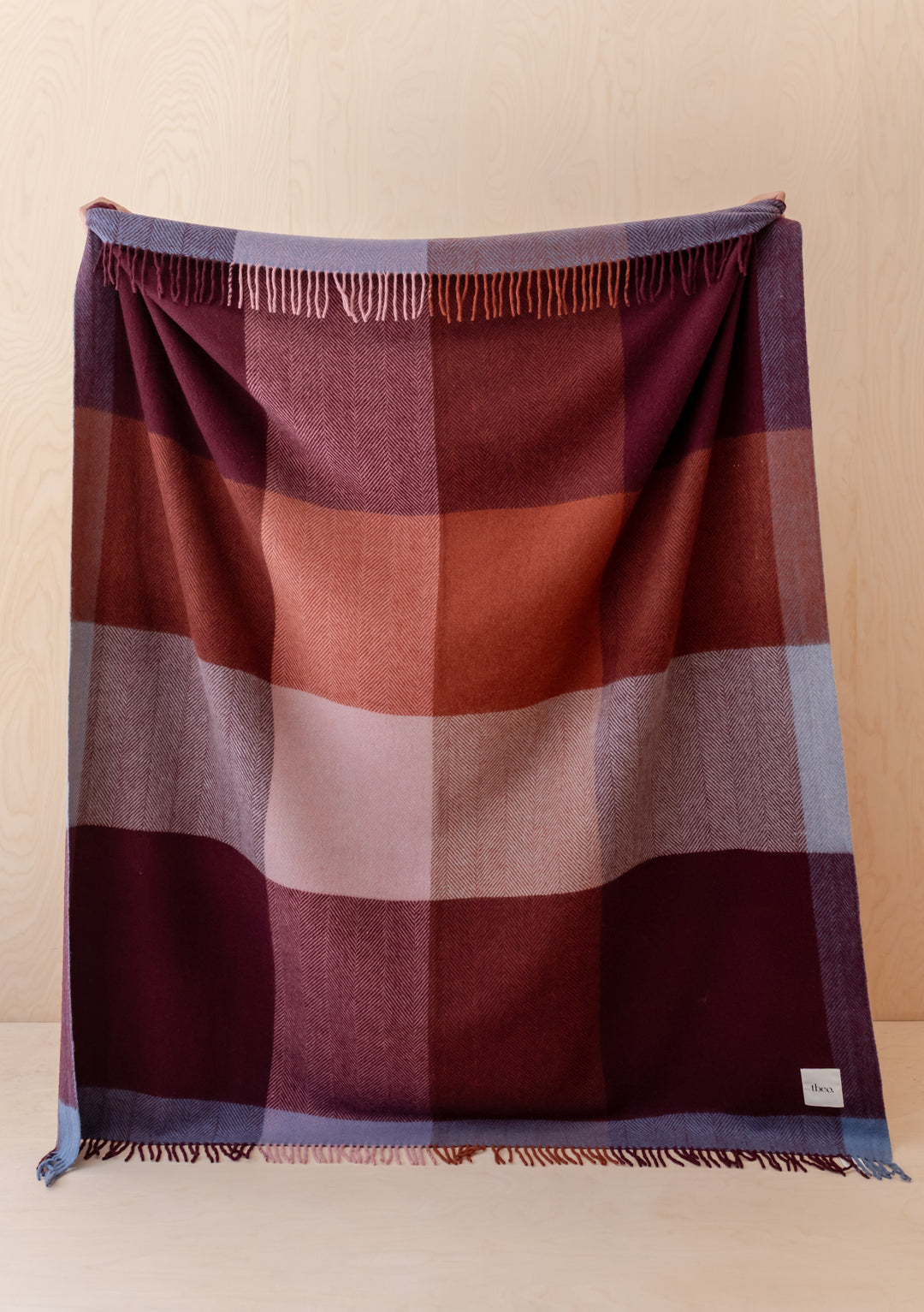 TBCo Recycled Wool Blanket in Berry Frame Check draped showing berry and burgundy tones with fringed edges.