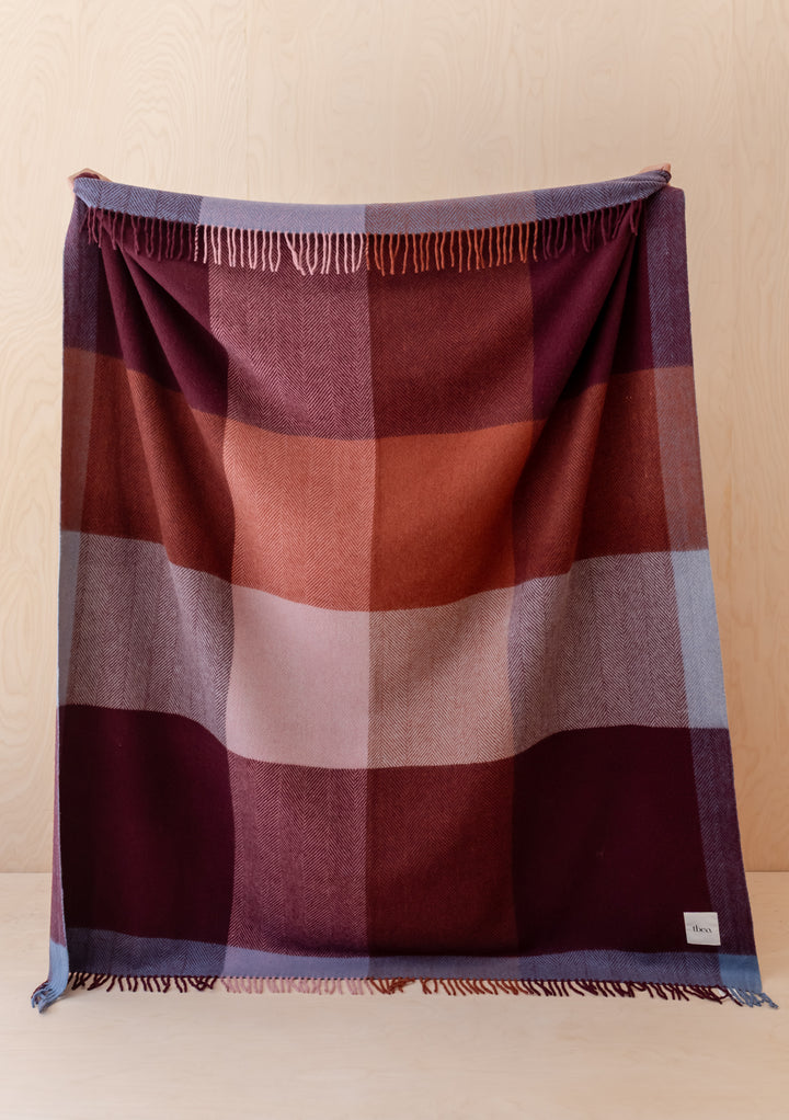 TBCo Recycled Wool Blanket in Berry Frame Check draped showing berry and burgundy tones with fringed edges.