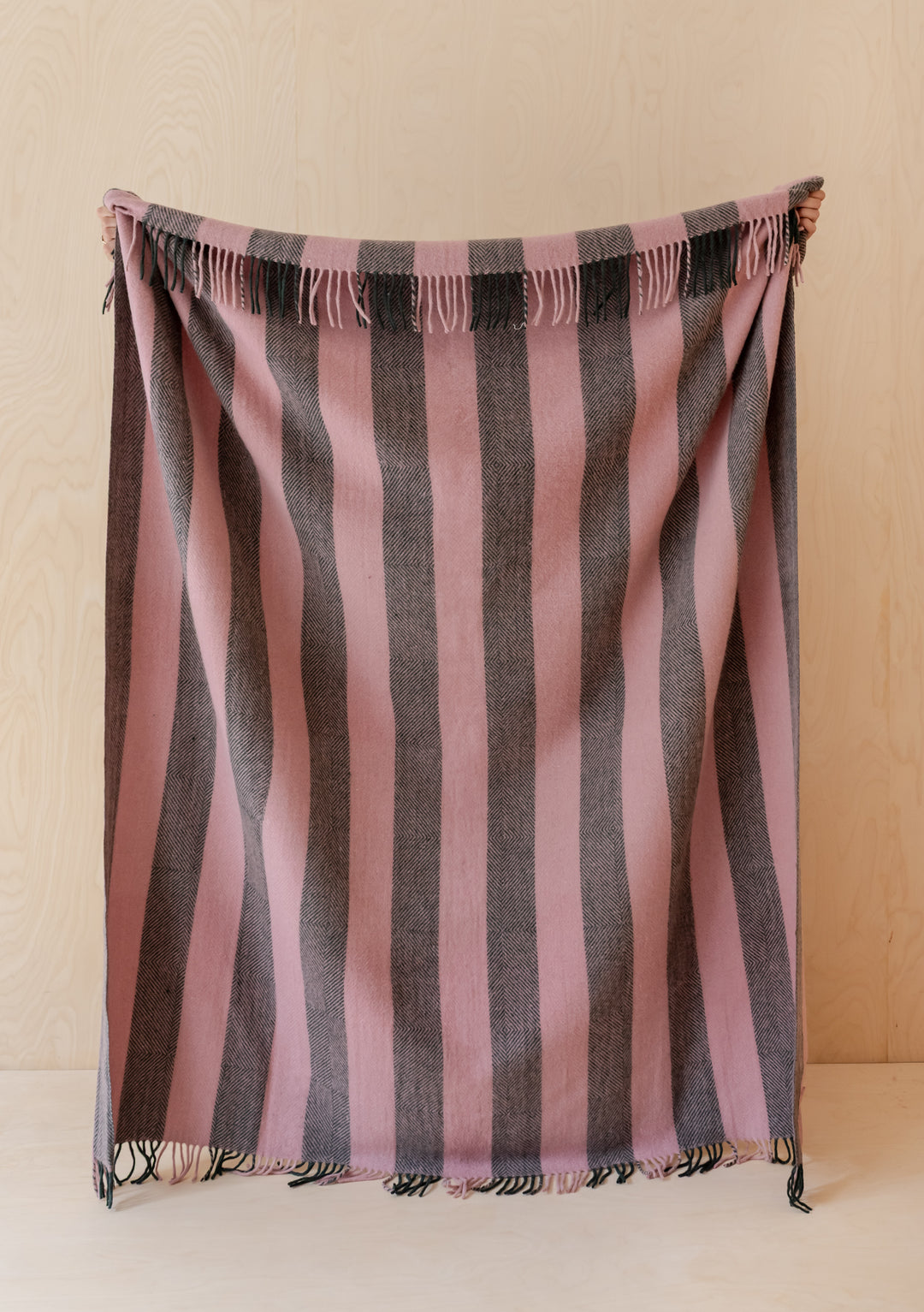 TBCo Recycled Wool Blanket in Pink Diamond Stripe with fringed edges hanging against a light wood background