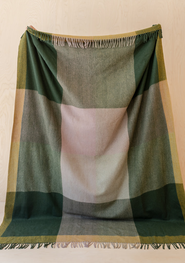 TBCo Recycled Wool Extra Large Blanket in Green Frame Check with fringed edges hanging against pale wood background