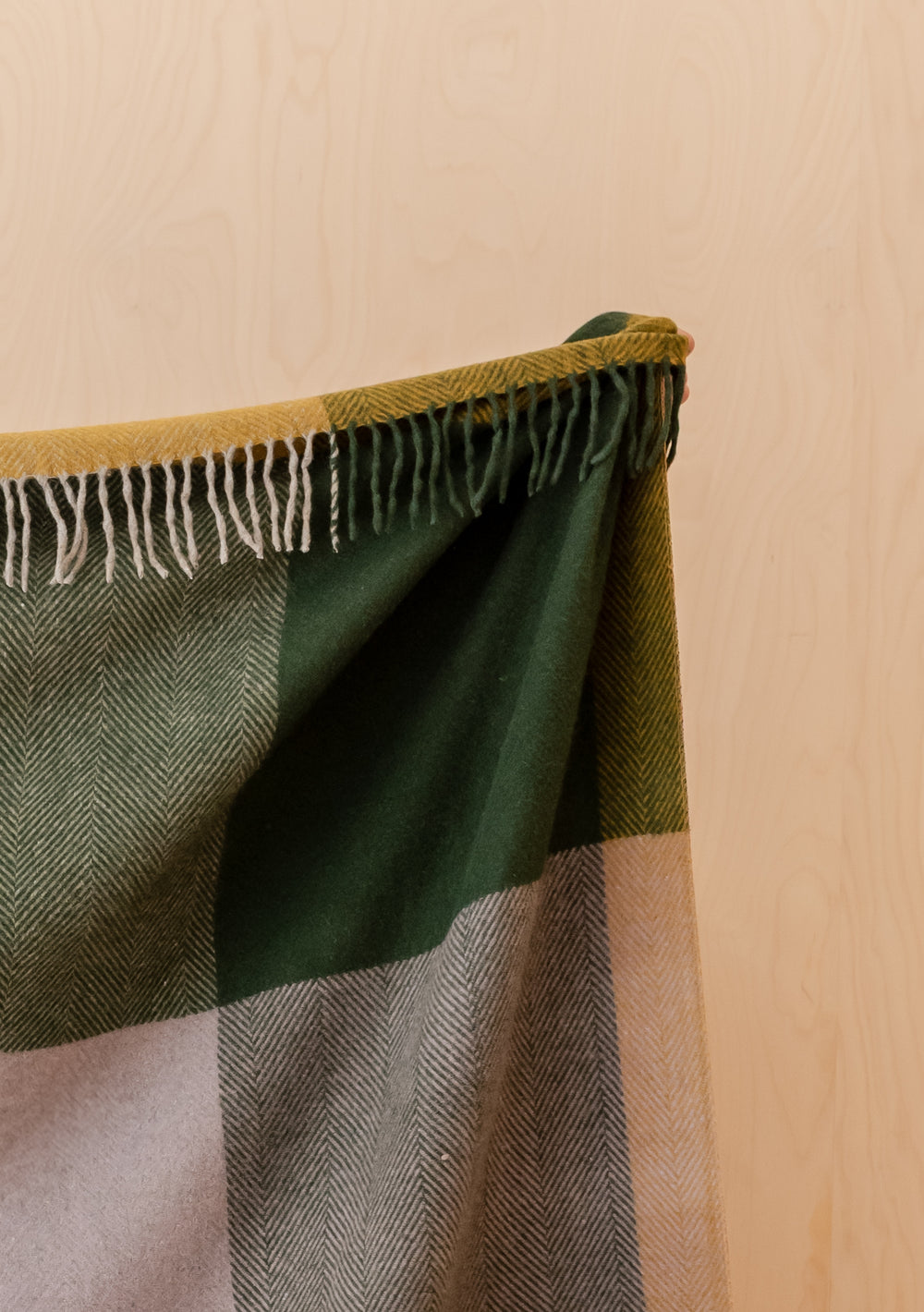 Fringed Recycled Wool Extra Large Blanket in Green Frame Check by TBCo hanging against a light wooden background