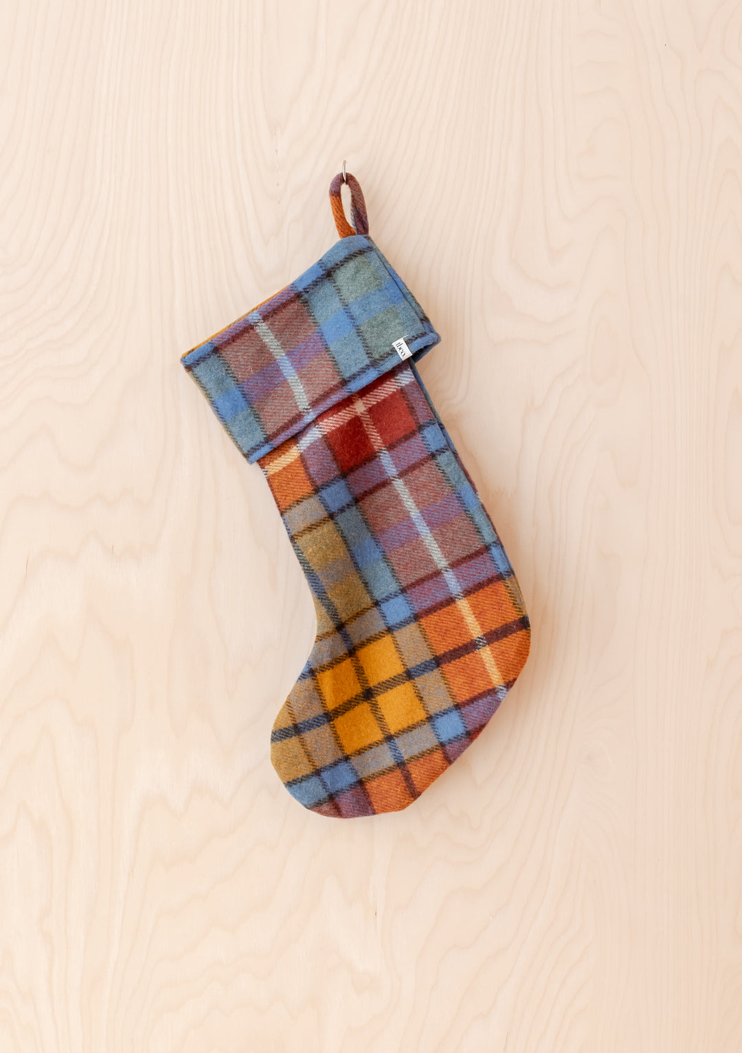 Recycled Wool Christmas Stocking in Buchanan Antique Tartan by TBCo hanging on wooden background in warm tones