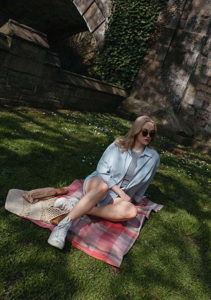 TBCo recycled wool picnic blanket in pink patchwork check displayed on grass, showcasing portable design and check pattern
