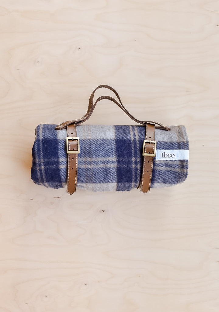 A TBCo recycled wool picnic blanket in Bannockbane Silver Tartan, rolled up and held in a leather TBCo picnic carrier.