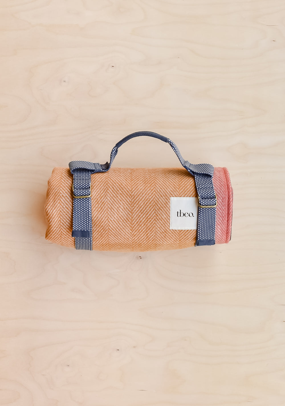 A TBCo recycled wool picnic blanket in mustard frame check, rolled up and held in a recycled plastic TBCo picnic carrier.