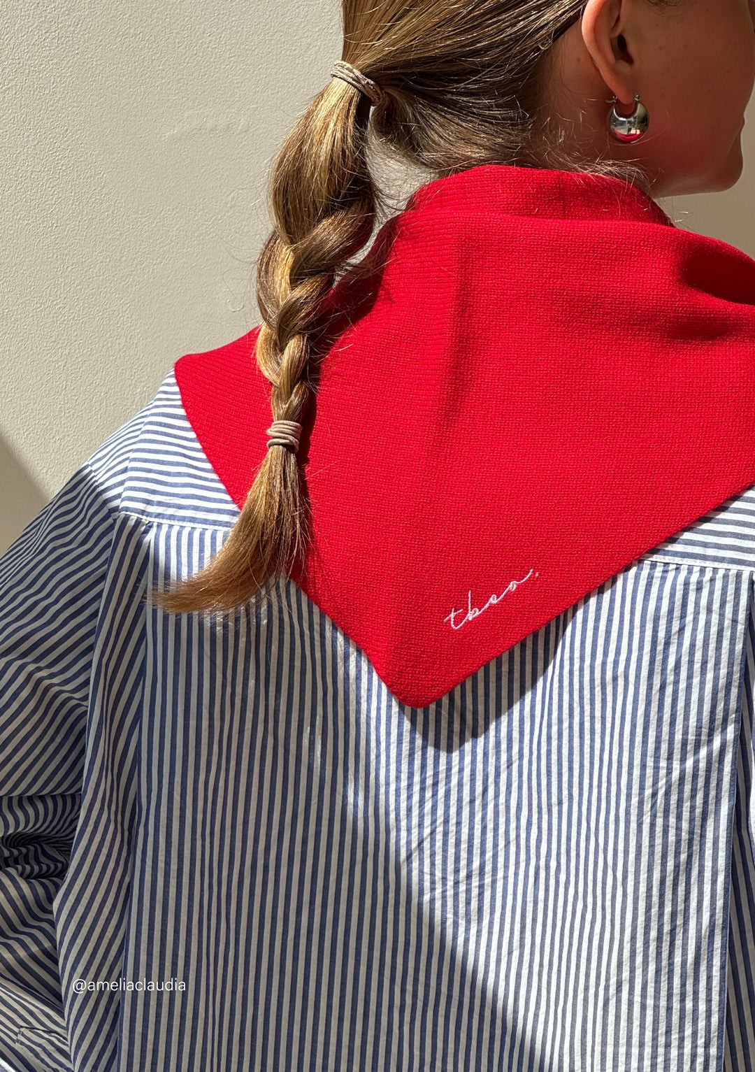 Woman wearing TBCo Merino Triangle Scarf in Red over striped shirt, embroidered logo visible on soft merino wool fabric