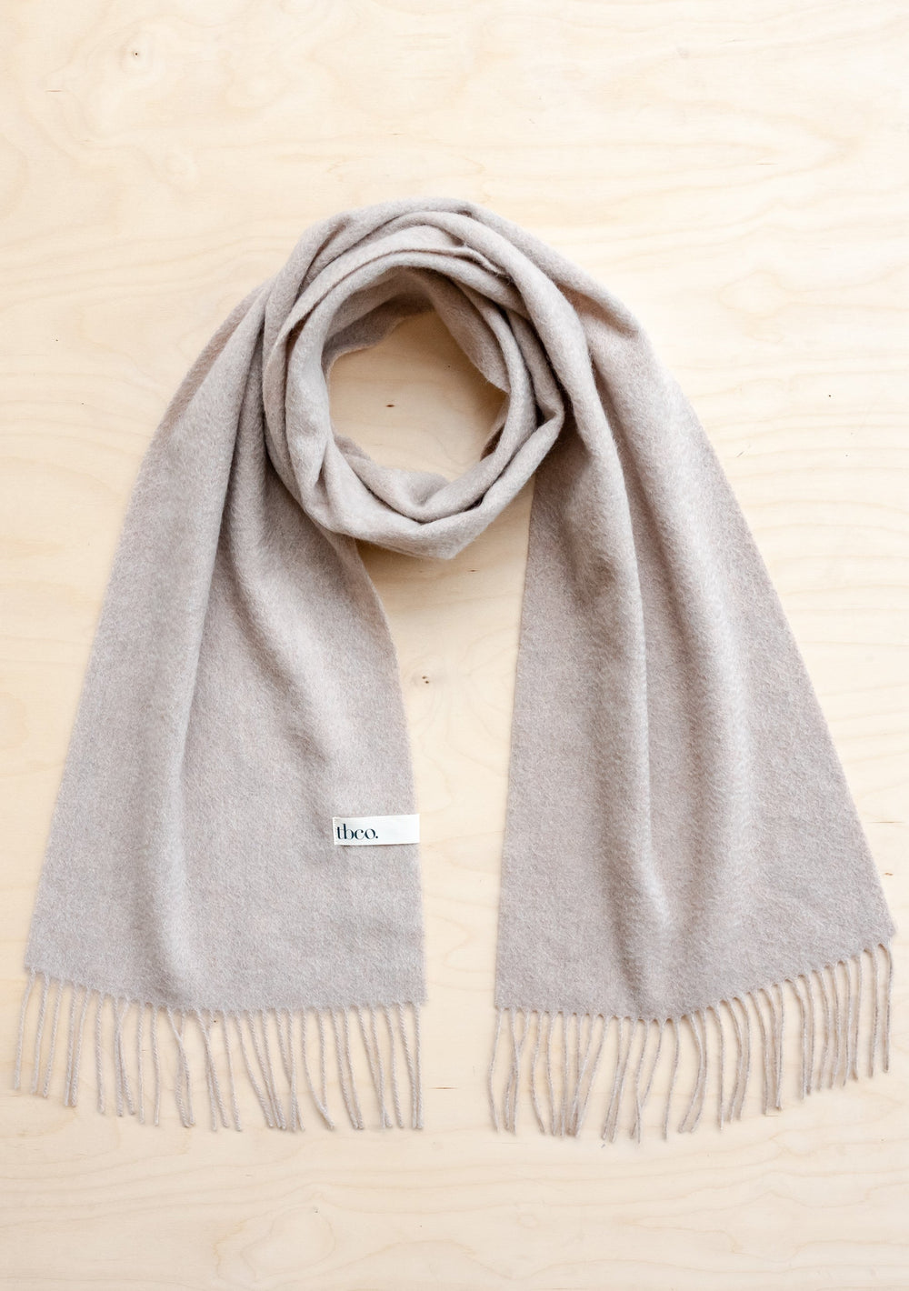 TBCo Men's Cashmere Scarf in Oatmeal Melange with fringed edges, luxuriously woven in pure cashmere, displayed flat on beige surface