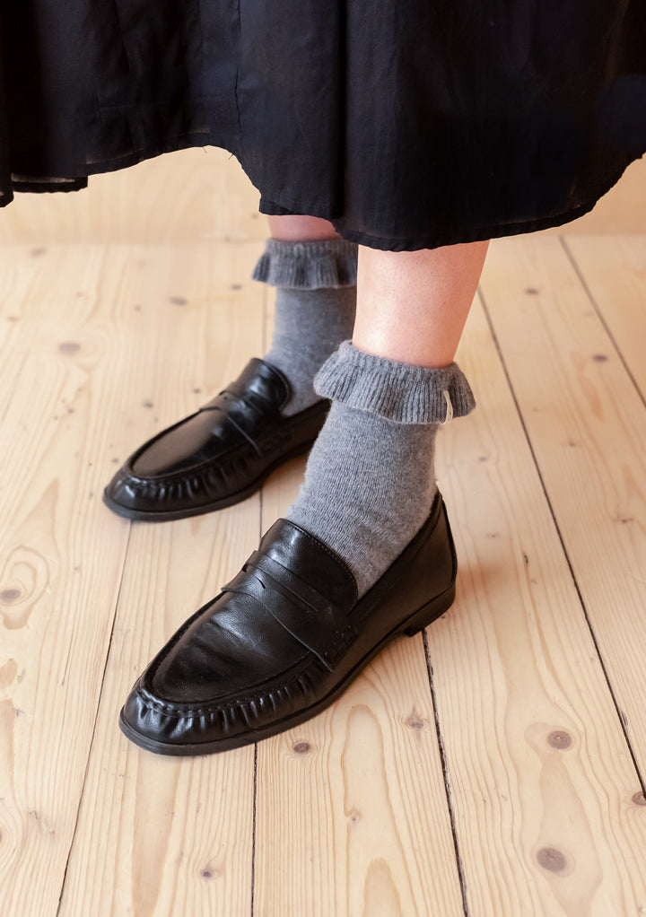 Feet wearing TBCo Merino Wool Socks in Charcoal Frilly paired with black loafers on wooden floor background
