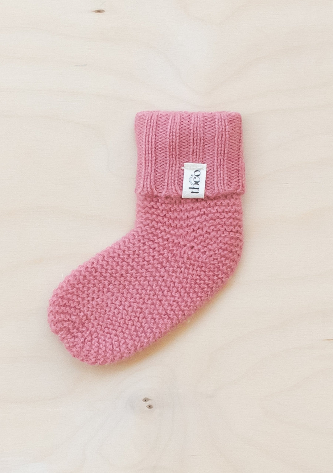 TBCo Merino Wool Baby Socks in Rose, knitted with ribbed cuff and textured stitch pattern on light wooden background