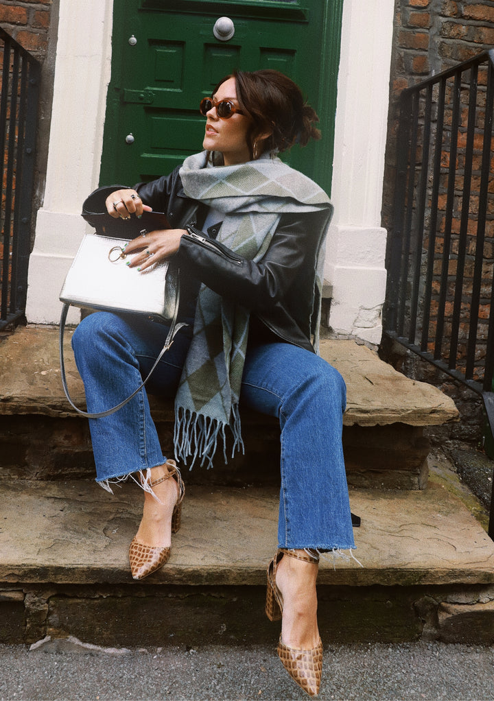 The TBCo x Amy Bell Dunnottar Scarf styled with leather jacket and jeans on stone steps by green door in Edinburgh