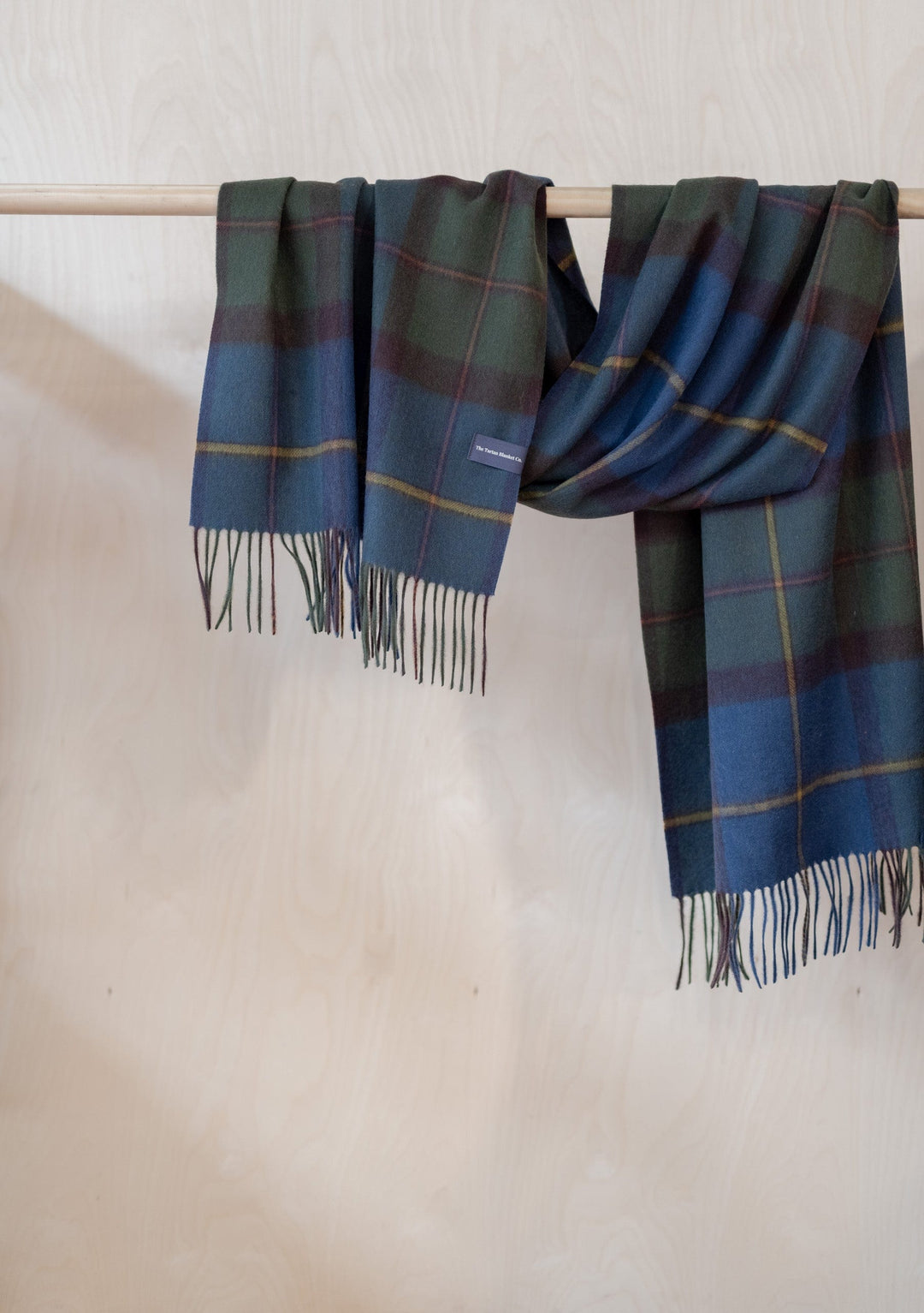 TBCo Lambswool Oversized Scarf in Macleod of Harris Antique Tartan with fringed edges, draped on wooden rail showing plaid pattern