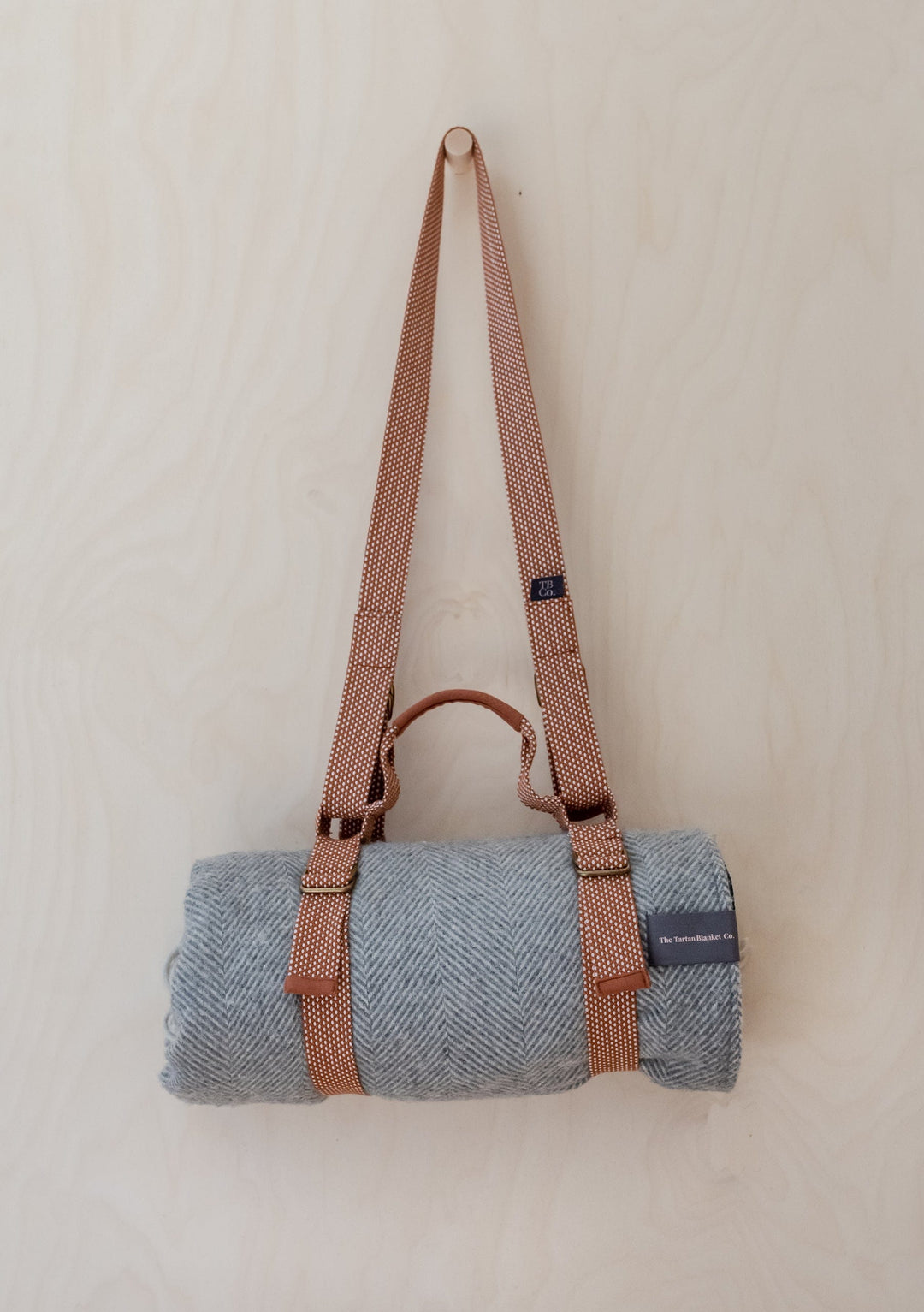 TBCo Recycled Picnic Carrier with brown adjustable shoulder strap and brass buckles holding rolled grey wool blanket