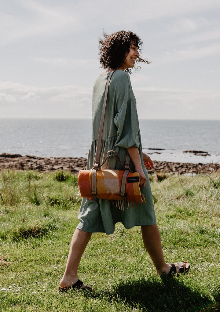 TBCo wool picnic blankets with carrier and should strap arranged in a scenic outdoor setting, showcasing their soft texture and vibrant patterns. Perfect for alfresco dining, relaxing in nature, or stylish outdoor gatherings.