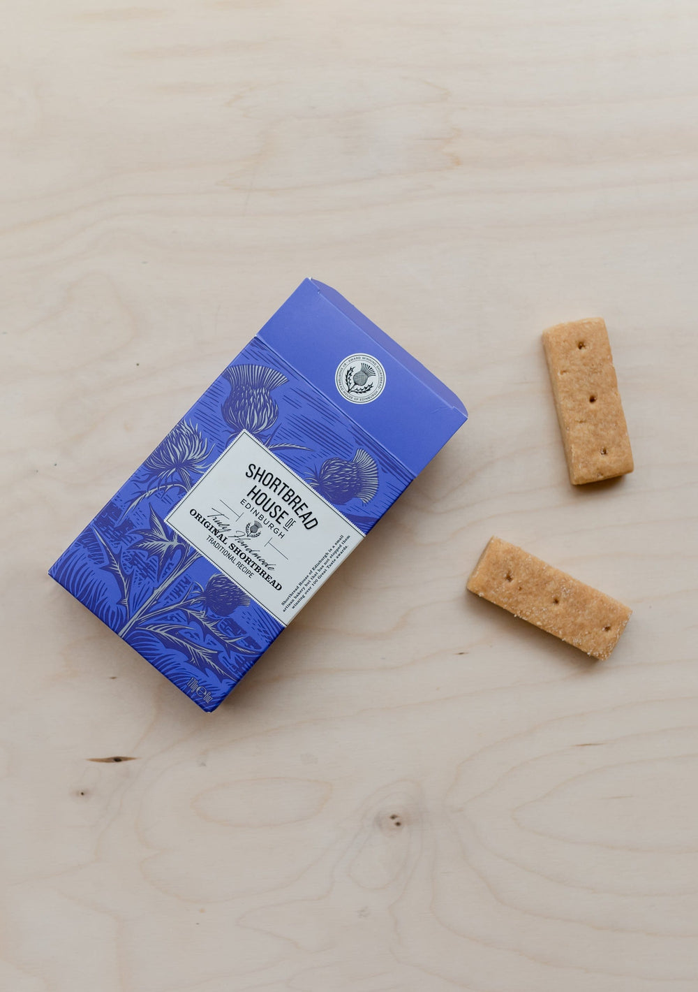 Traditional TBCo Shortbread Fingers in blue box with two biscuits displayed on wooden surface