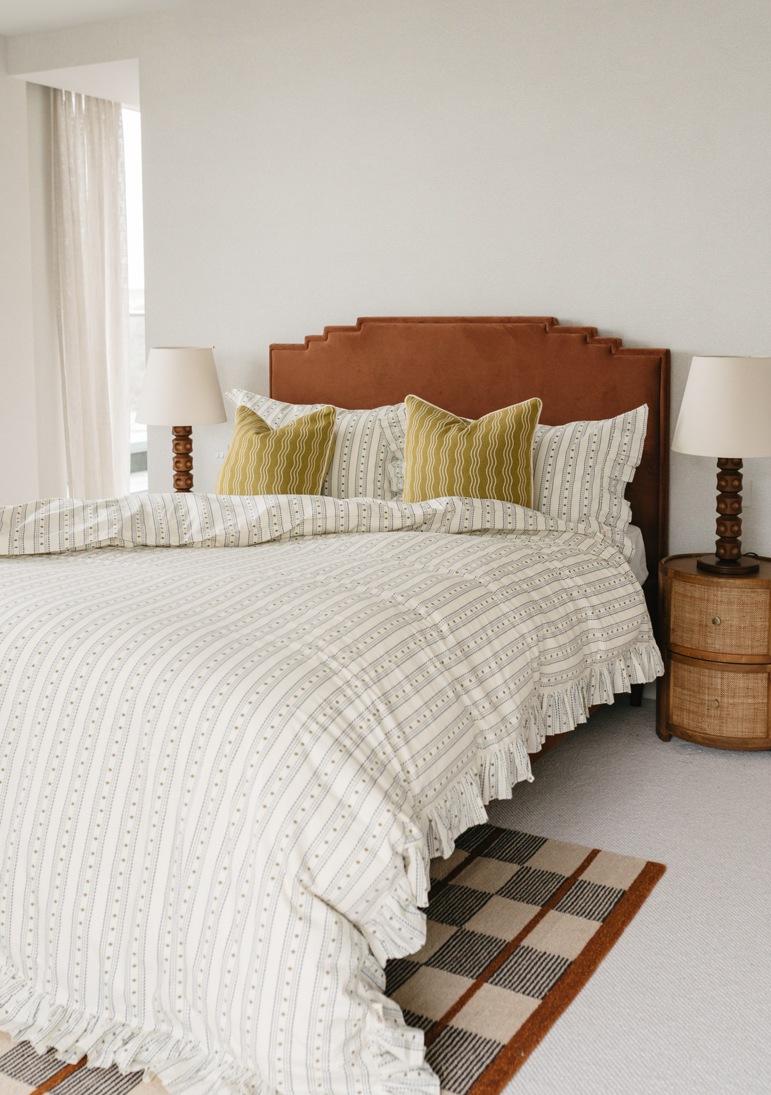 TBCo Bedding Set featuring striped white duvet with ruffled edges, mustard accent pillows and brown leather headboard