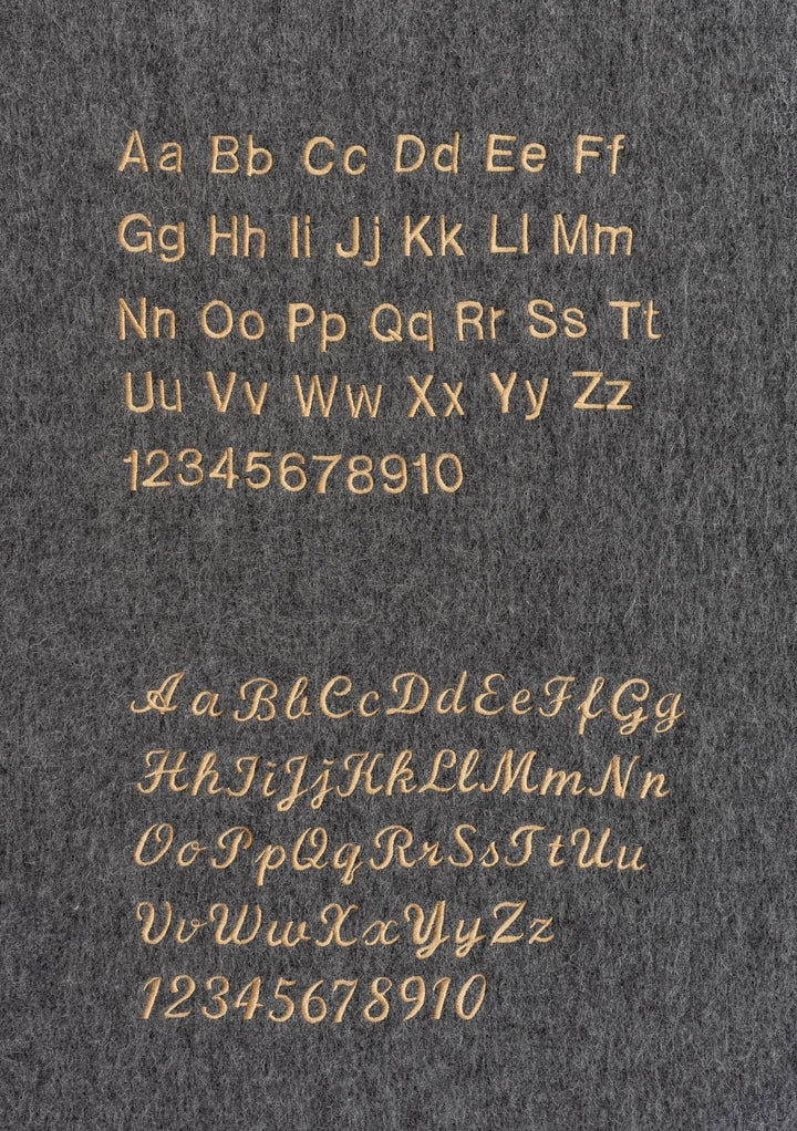 Custom embroidery options on grey fabric showcasing letter styles for the Merino Wool Triangle Scarf in Blue & Brown Stripe by TBCo
