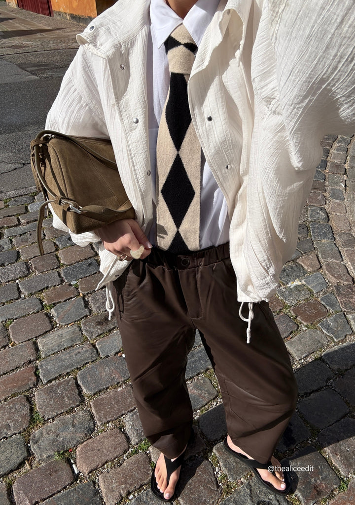 Person wearing TBCo Merino Wool Skinny Scarf in Black Harlequin styled with white jacket and dark trousers on cobblestone street