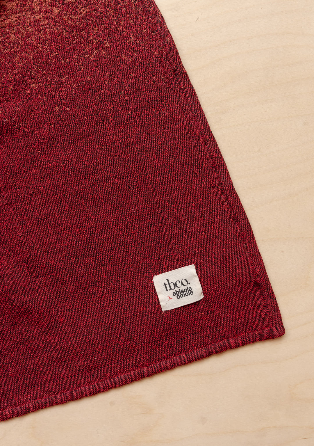 TBCo x Abisola Omole Hues Cotton Throw featuring gradient burgundy tones and charcoal, with signature TBCo label detail