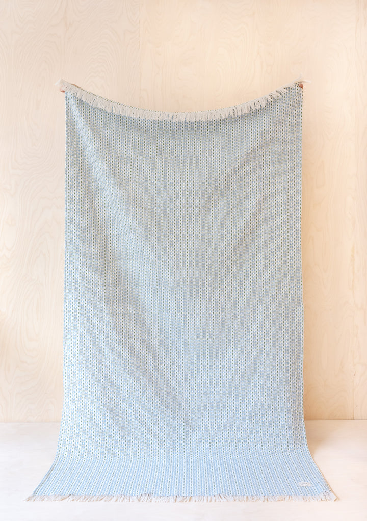 Sustainable TBCo Cotton Throw in Green Geometric with detailed jacquard pattern, displayed hanging against cream wall