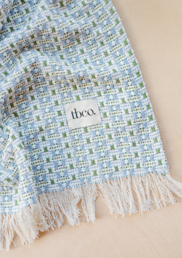 TBCo Cotton Throw in Green Geometric pattern featuring delicate blue and white jacquard weave with fringed edges and signature label