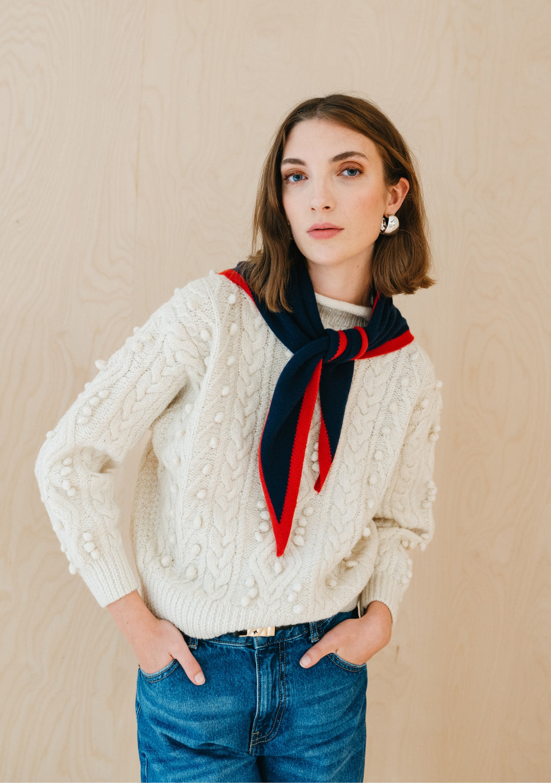 Model wearing TBCo Merino Triangle Scarf in Navy & Red styled with a cream knit sweater and blue jeans indoors