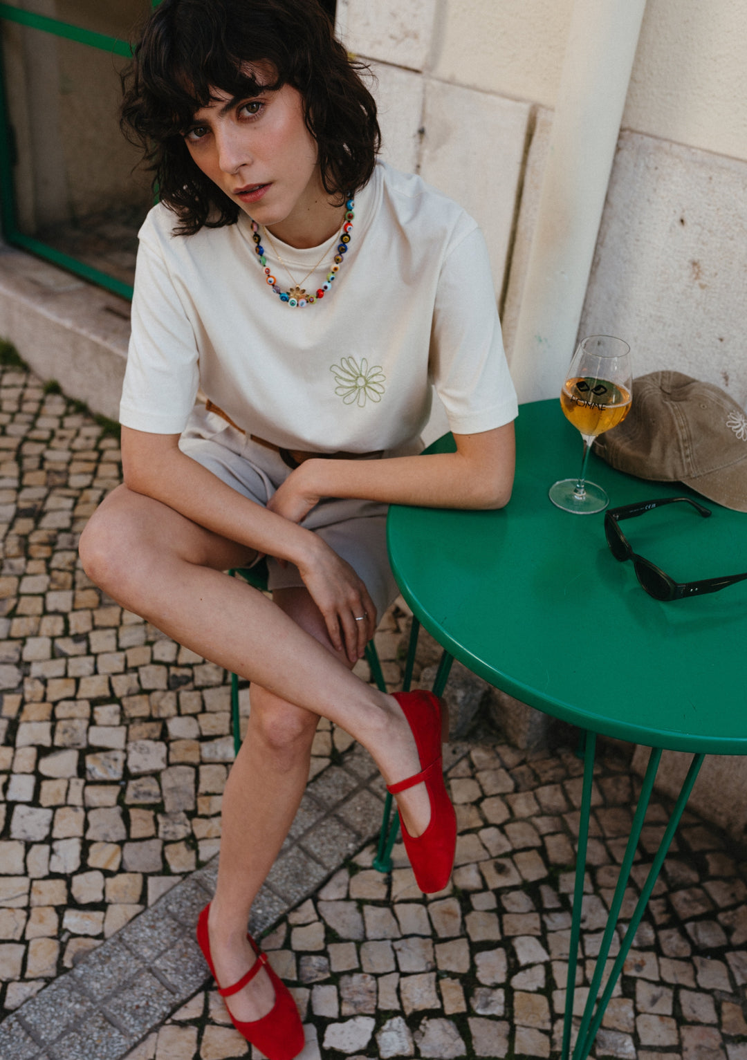 TBCo Cotton T-Shirt in Ecru Flora with embroidered daisy and floral checkerboard design, shown styled with red shoes at cafe table