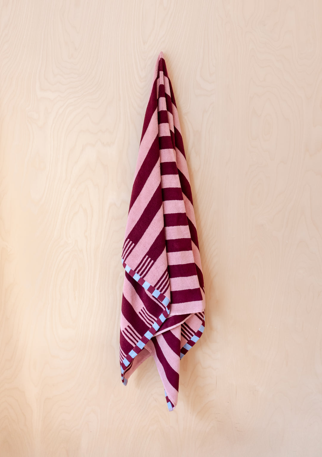 TBCo Cotton Towels in Pink Stripe with burgundy stripes and blue checkered border, hanging elegantly against cream wall