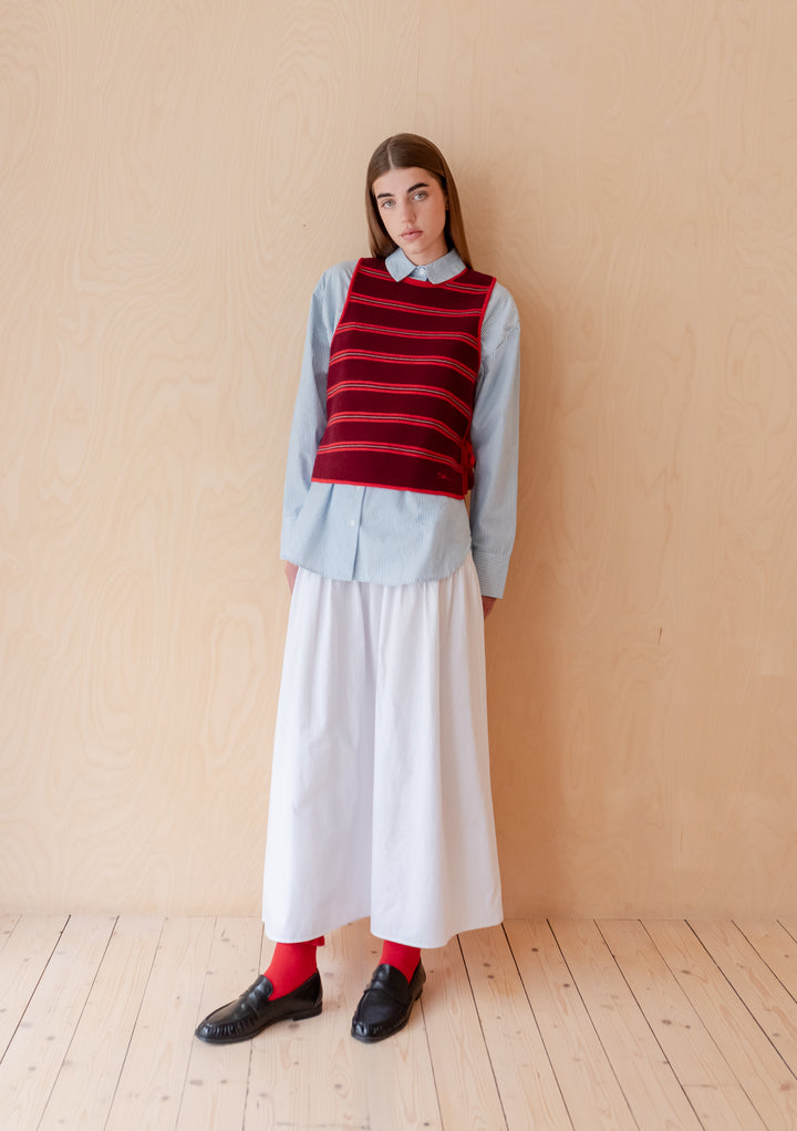 Model wearing TBCo Merino Wool Tie Vest in Burgundy Stripe over blue shirt with white skirt and black shoes
