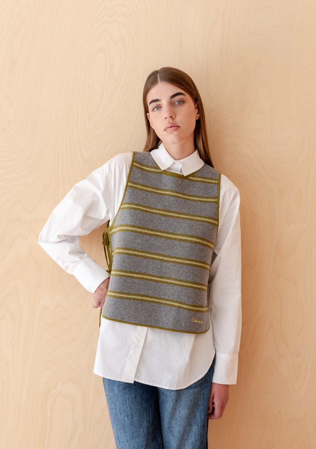 Woman wearing TBCo Merino Wool Tie Vest in Green Stripe over white shirt and jeans against wooden background