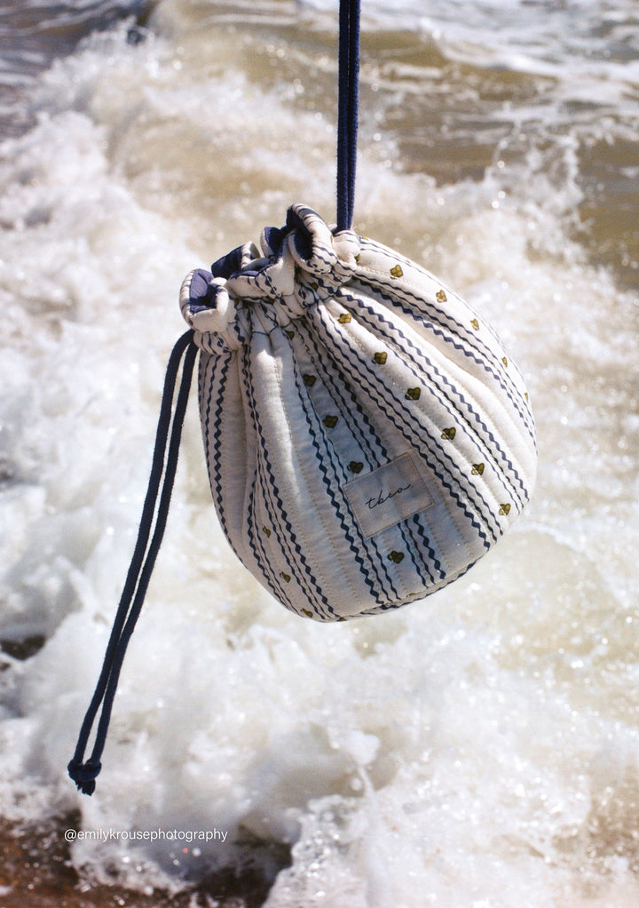 TBCo Cotton Wash Bag in Navy Ditsy Floral hanging by drawstring with waves crashing in the background