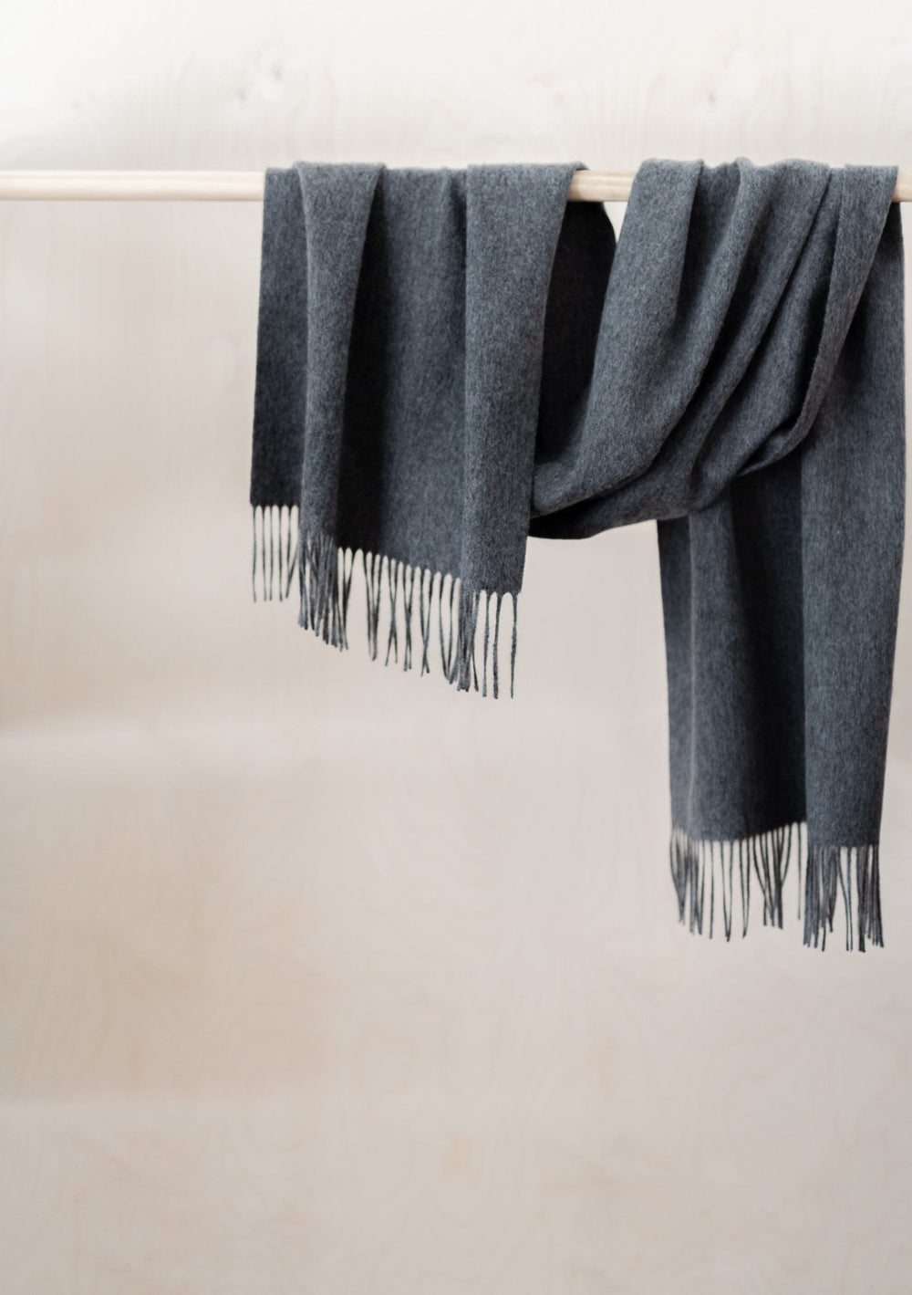 TBCo Lambswool Oversized Scarf in Charcoal Melange draped elegantly over wooden rail showing fringed detail and soft texture