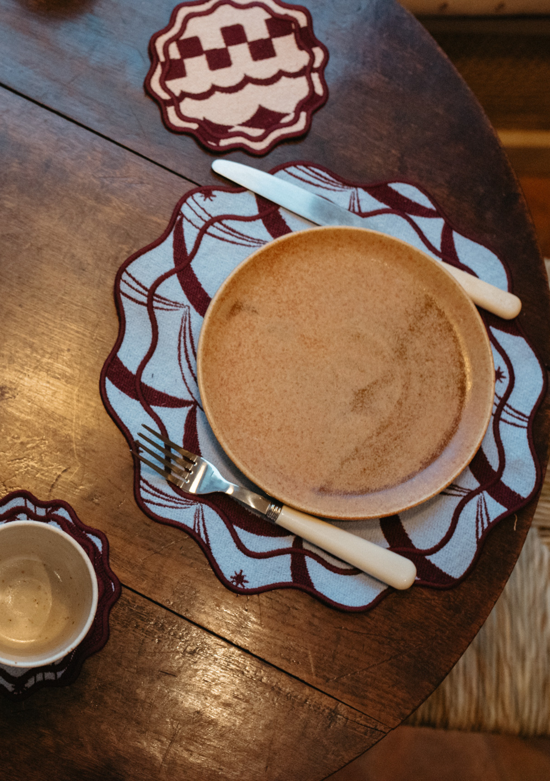 TBCo Tableware Set featuring patterned placemats and coasters with a minimalist plate and cutlery on a wooden table.