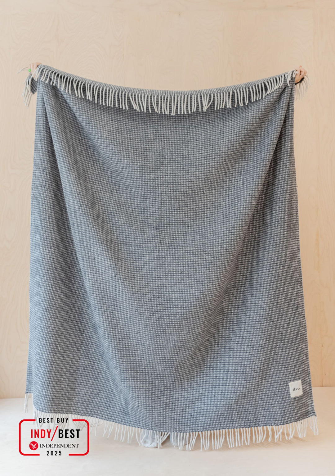 TBCo Recycled Wool Blanket in Charcoal Waffle pattern displayed with fringe detail against cream wall, showing textured weave