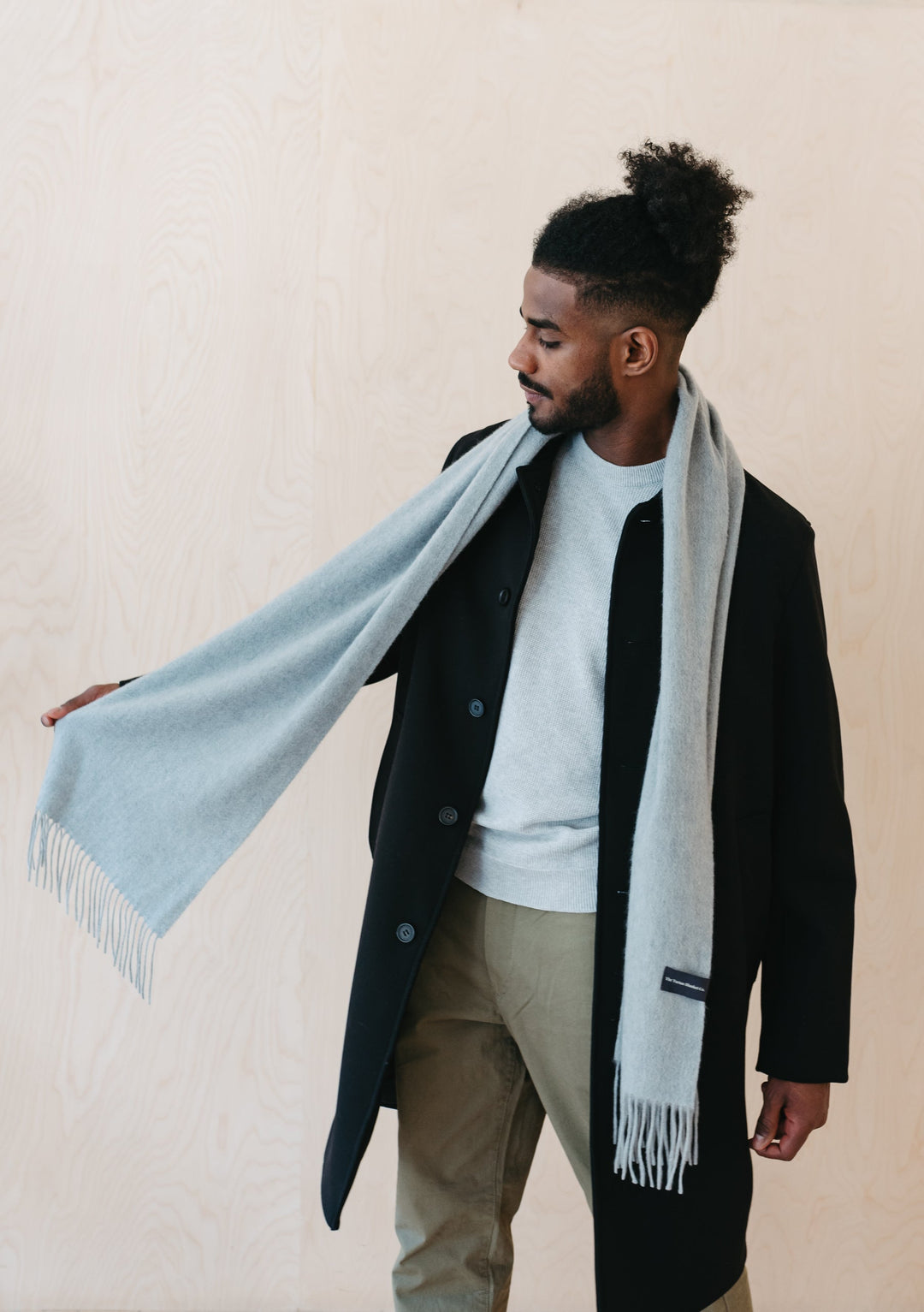 TBCo light grey melange cashmere men's scarf with fringe elegantly draped over black winter coat showing luxurious texture