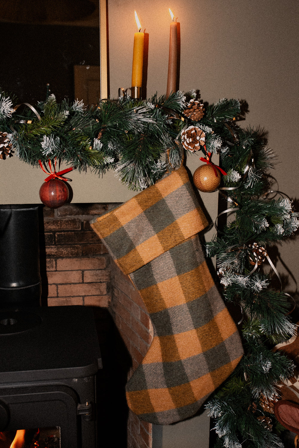 Cozy Recycled Wool Christmas Stocking in Jacob Tartan by TBCo hanging on festive garland above fireplace.