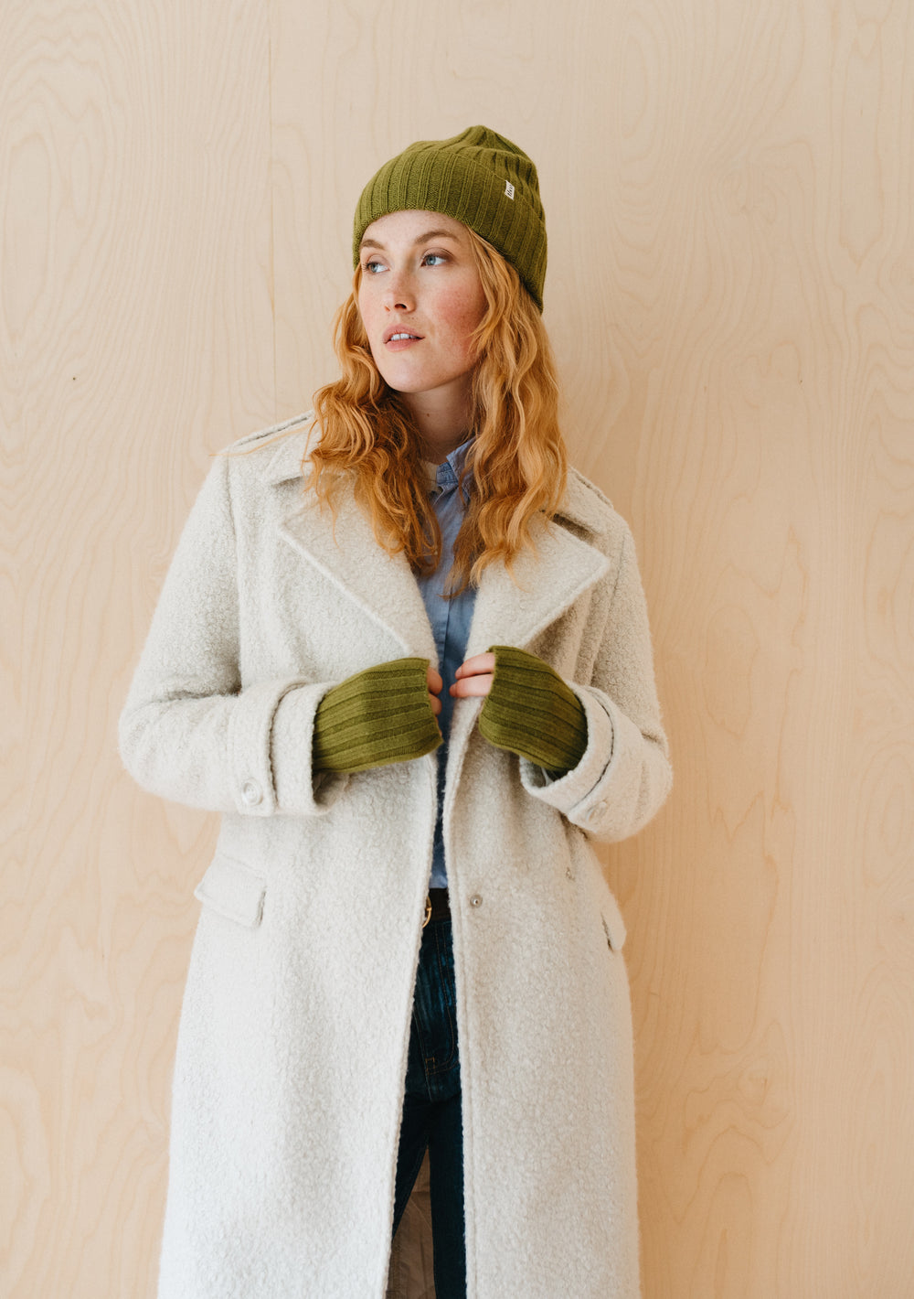 TBCo Cashmere & Merino Beanie in Olive styled with cream winter coat and matching olive gloves against wooden backdrop