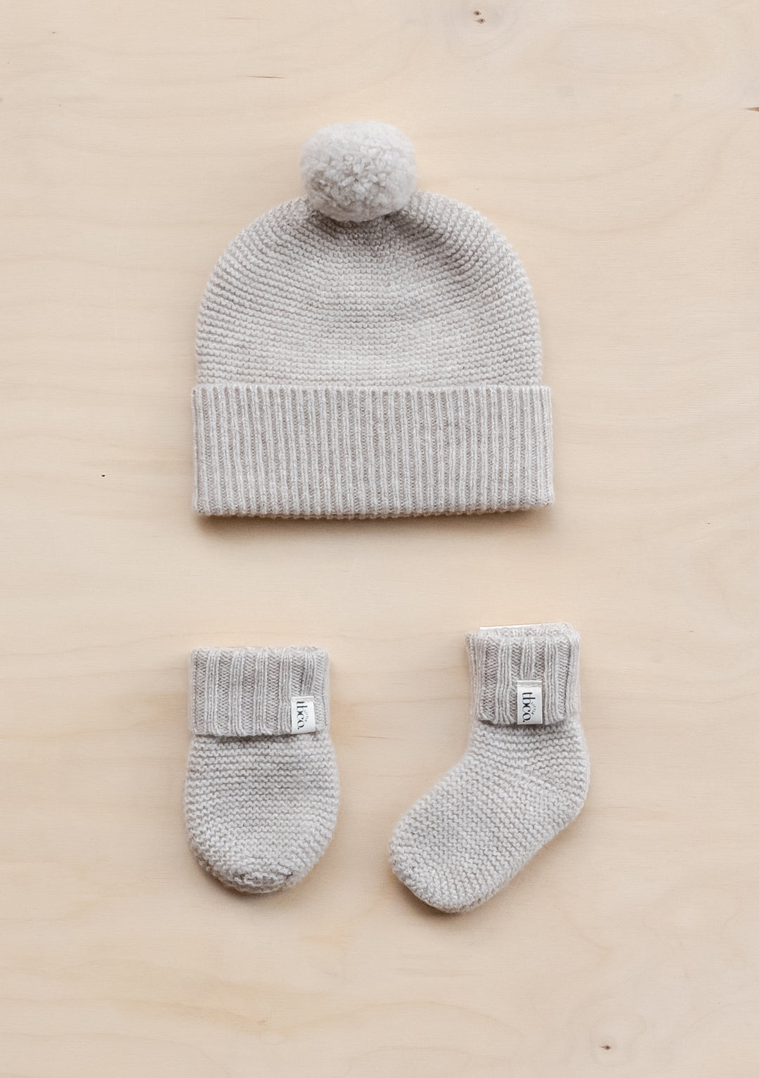 TBCo Merino Wool Baby Accessories Bundle in oatmeal melange featuring knitted beanie with pom-pom, cosy mittens and socks