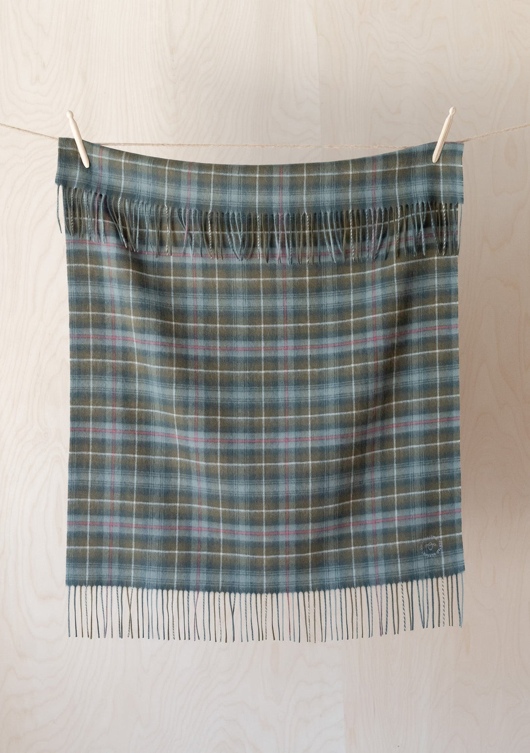 TBCo Lambswool Baby Blanket in Mackenzie Weathered Tartan hanging on clothesline showing fringed edge and plaid pattern