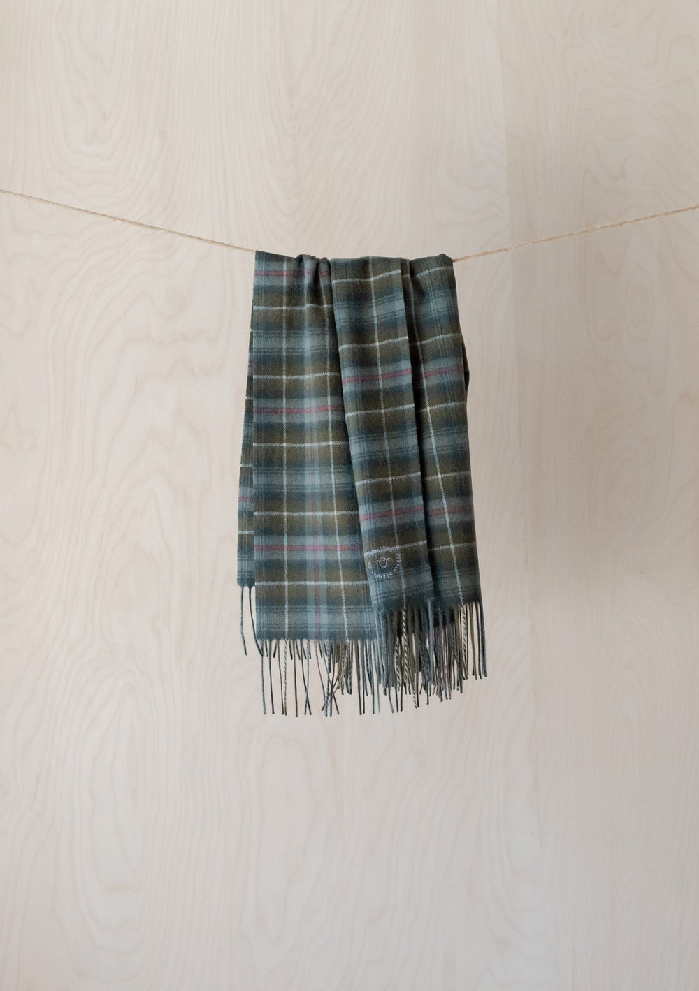 TBCo Mackenzie Weathered Tartan Lambswool Baby Blanket hanging on string, showing fringed edge and traditional plaid pattern