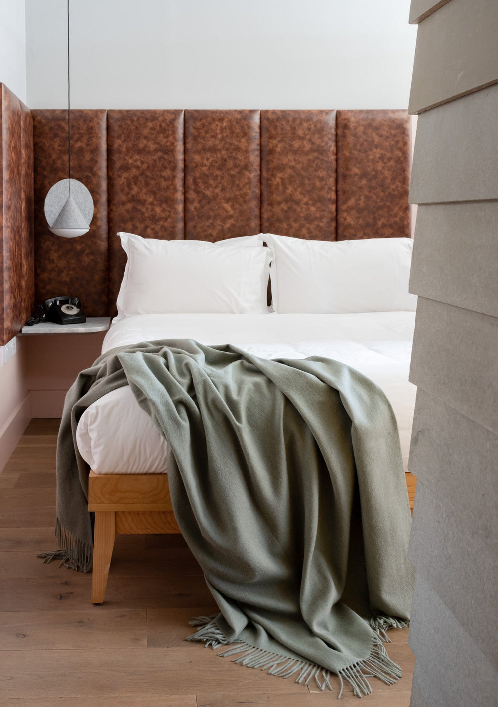 TBCo Sage Melange Lambswool Blanket draped over white bedding in modern bedroom with brown leather headboard