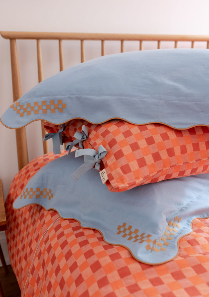 Bedding Set featuring blue scalloped pillowcases with orange checkered pattern and bow ties against wooden headboard